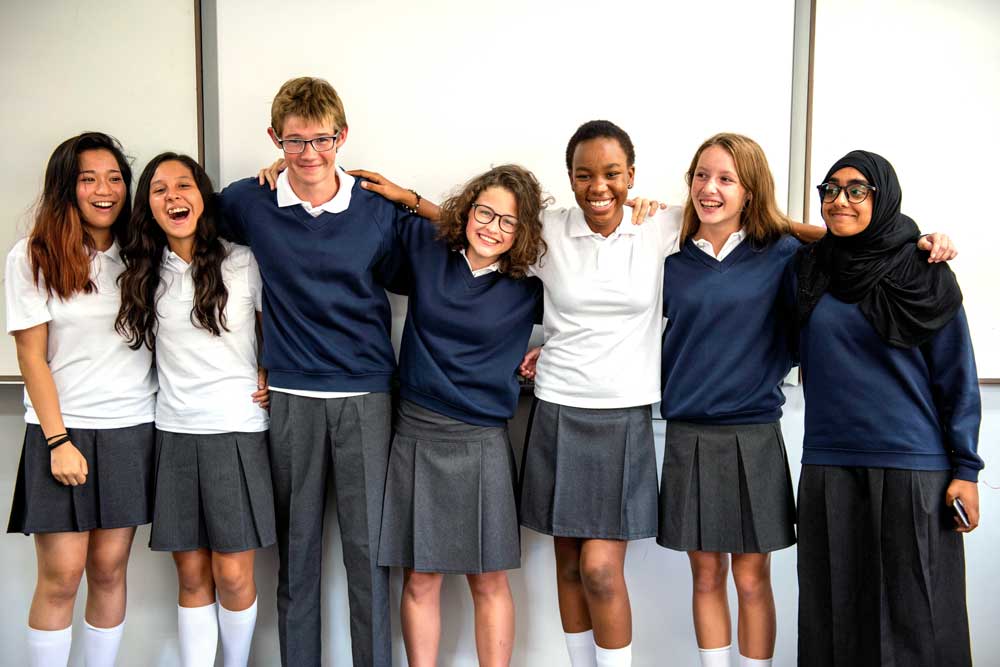 a group of students at school from diverse backgrounds with their arms on each others shoulders and smiling